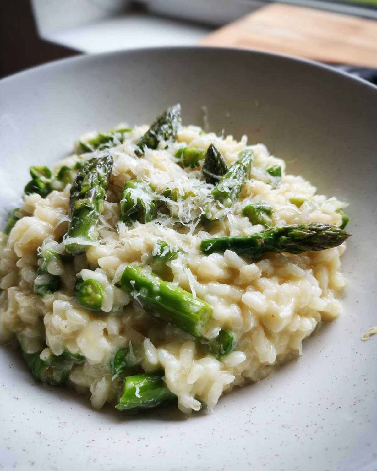 A close-up of Easy Creamy Asparagus Risotto topped with vibrant green asparagus pieces and grated Parmesan cheese in a light bowl.