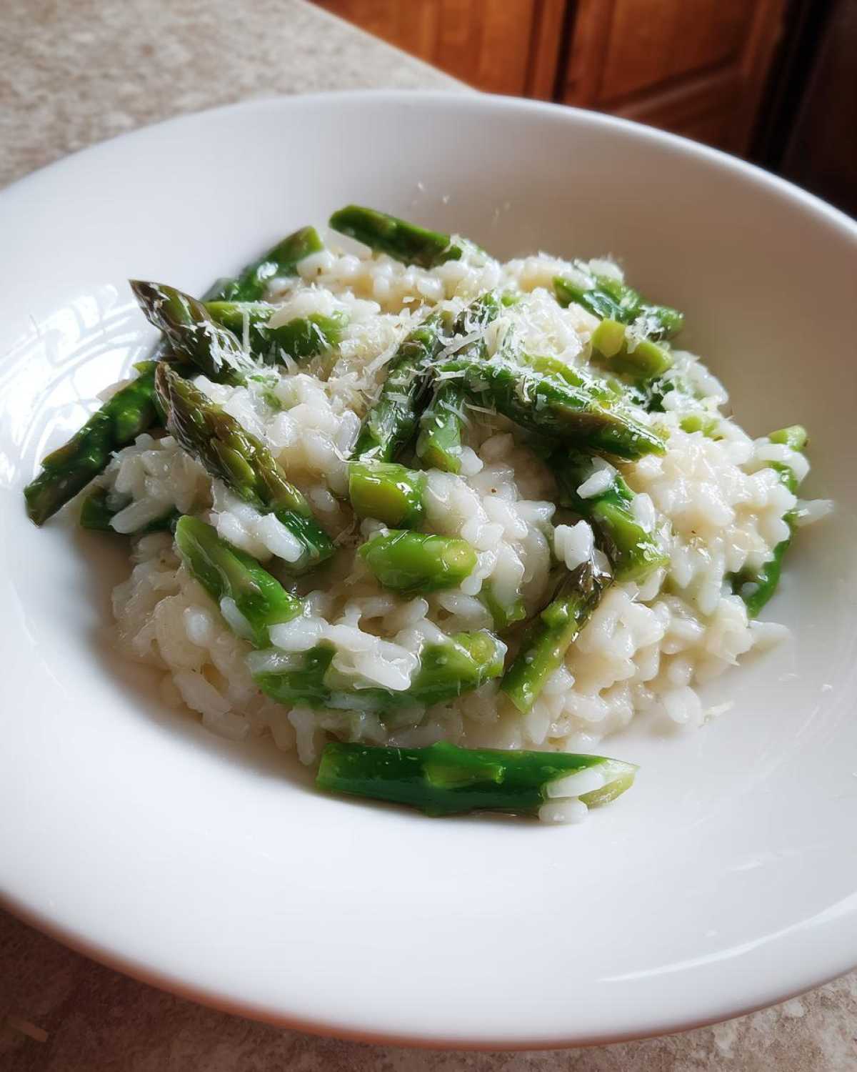 A close-up of a white bowl filled with Easy Creamy Asparagus Risotto topped with grated cheese.