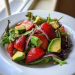 Close-up of a vibrant Easy Strawberry Avocado Salad featuring sliced strawberries, avocado chunks, red onion, and mixed greens.