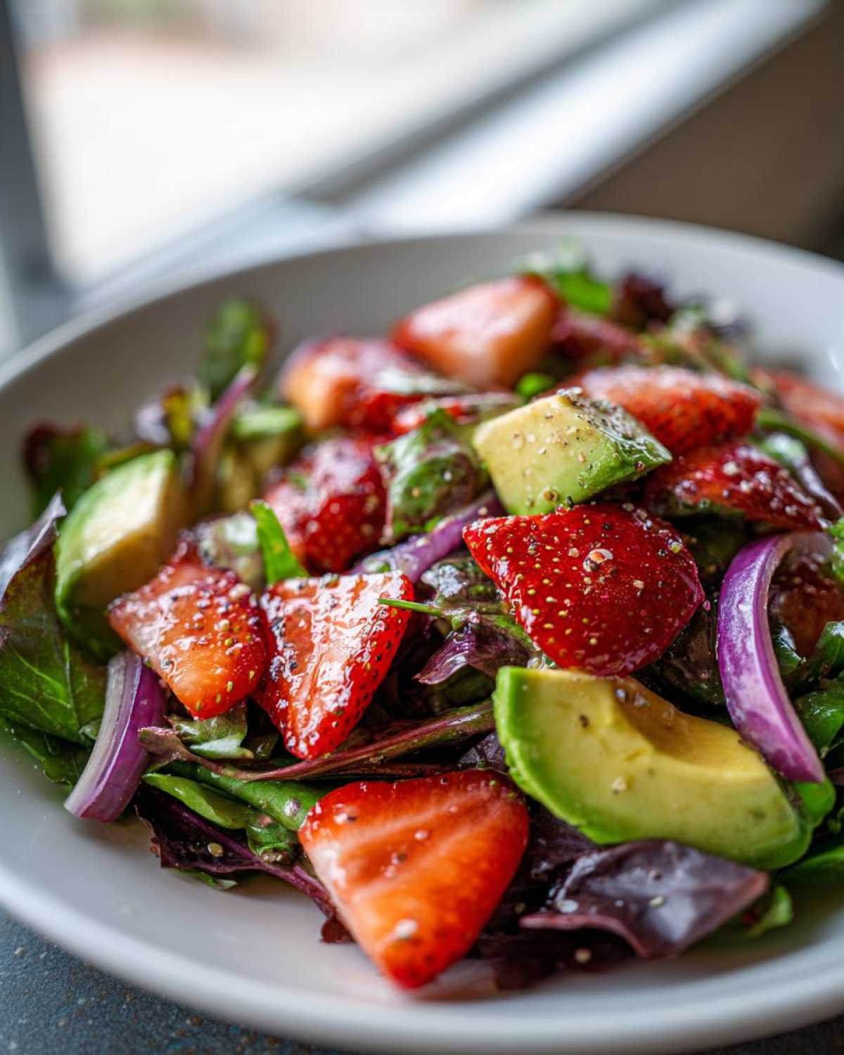 Close-up of a vibrant Easy Strawberry Avocado Salad featuring sliced strawberries, avocado chunks, and red onion on mixed greens.