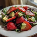 Close-up of an Easy Strawberry Avocado Salad featuring sliced strawberries, diced avocado, red onion, and mixed greens.