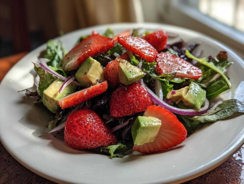 Close-up of an Easy Strawberry Avocado Salad featuring sliced strawberries, diced avocado, red onion, and mixed greens.