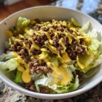 A close-up of a fresh big mac salad featuring lettuce, ground beef, pickles, and a drizzle of special sauce in a white bowl.