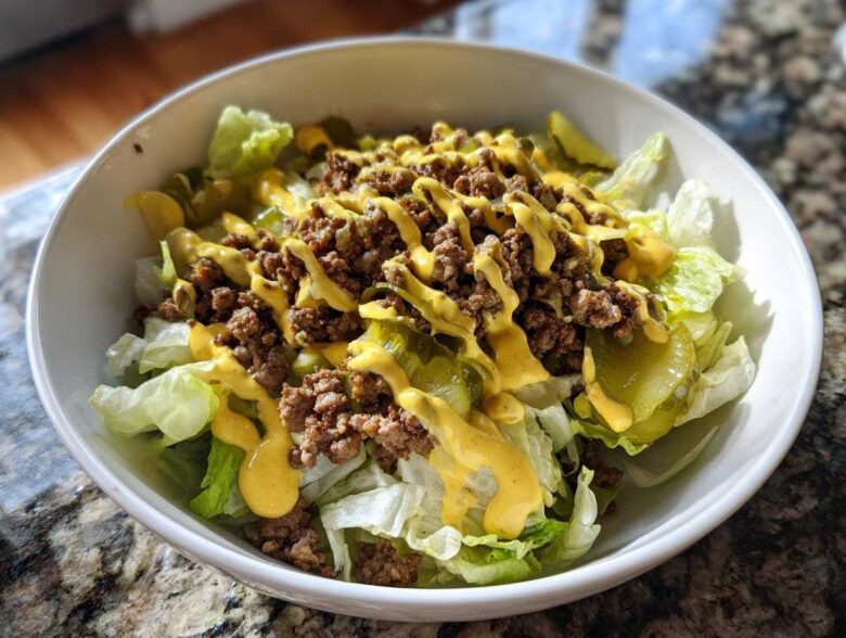 A close-up of a fresh big mac salad featuring lettuce, ground beef, pickles, and a drizzle of special sauce in a white bowl.