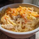Close-up of a white bowl filled with creamy, baked chicken spaghetti topped with melted, golden-brown cheese.