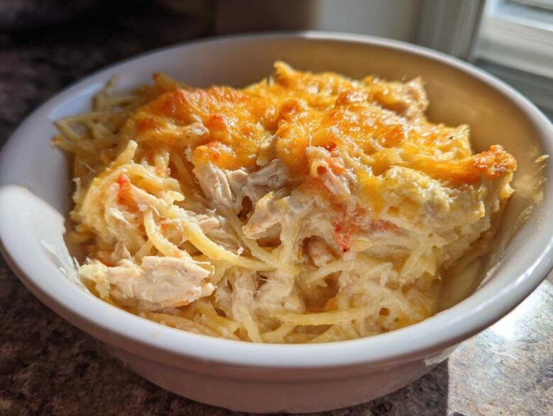 Close-up of a white bowl filled with creamy, baked chicken spaghetti topped with melted, golden-brown cheese.