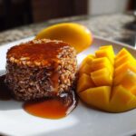 A molded serving of sticky rice topped with rich brown sauce, served next to a beautifully sliced mango, representing mango sticky rice.