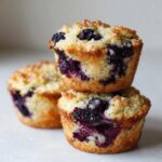 A stack of three fluffy blueberry cottage cheese muffins with a sugary top, showing juicy blueberries inside.