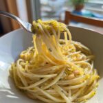 A fork lifting creamy pasta heavily topped with bright yellow lemon zest from the One-Pot Creamy White Bean Lemon Pasta.
