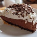 A close-up of a decadent slice of french silk pie featuring a dark chocolate filling, whipped cream, and chocolate shavings.