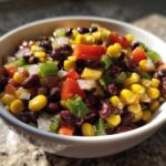 Close-up of a white bowl filled with vibrant cowboy caviar recipe featuring black beans, corn, tomatoes, and peppers.