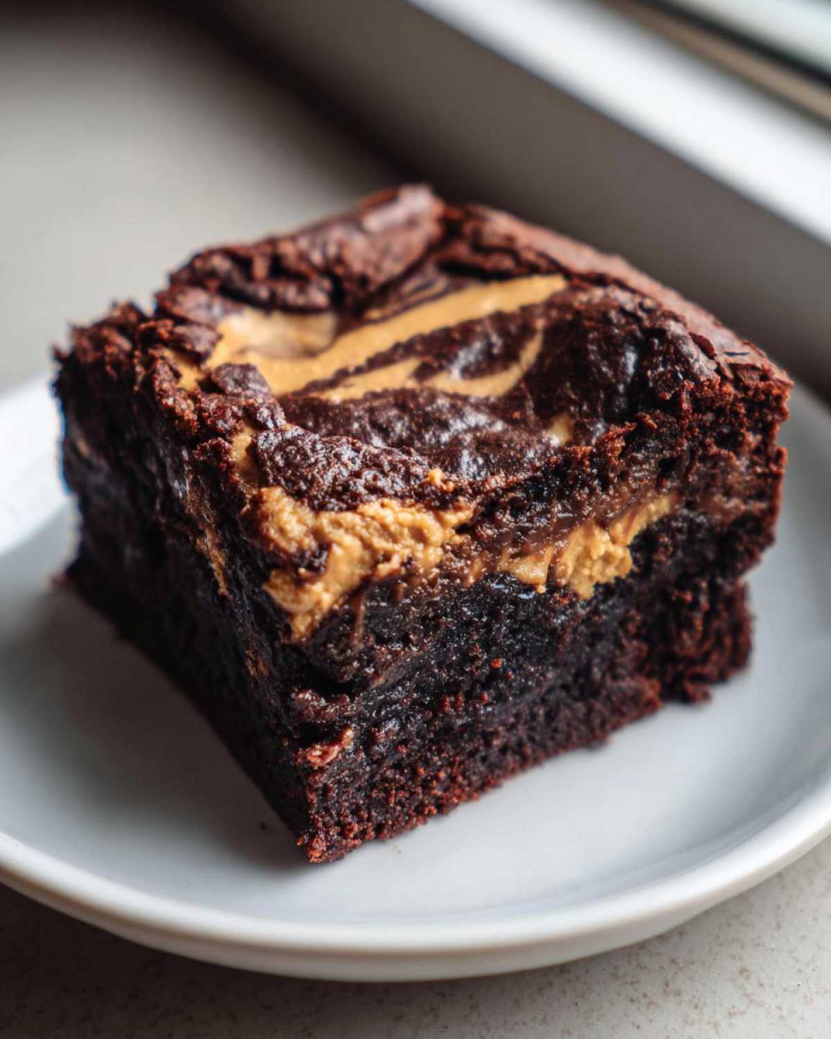 A close-up of a rich, fudgy peanut butter swirl brownies square served on a small white plate.