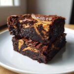 Two rich, fudgy peanut butter swirl brownies stacked on a white plate, showing the gooey peanut butter marbling.