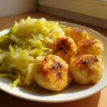 Five pan-fried German dumplings served next to a portion of buttered cabbage on a white plate.