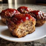 A close-up shot showing four glazed mini meatloaf portions, with one cut in half revealing the moist interior texture.