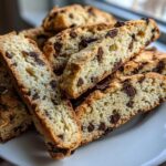 Close-up of several slices of golden Gluten-Free Chocolate Chip Biscotti stacked on a white plate.