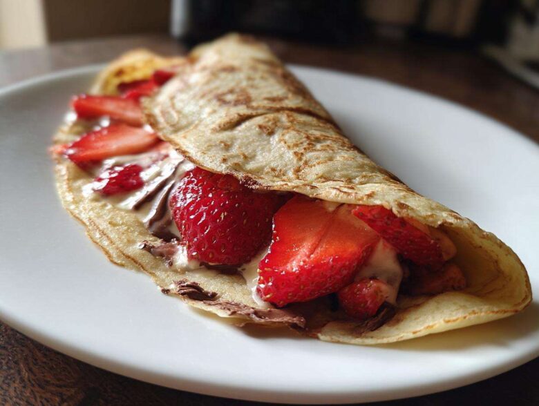 A folded Gluten-Free Chocolate Strawberry Crepes filled with fresh strawberries and chocolate spread on a white plate.