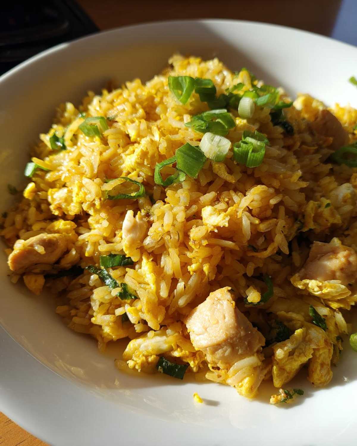 Close-up of a bowl filled with yellow Gluten-Free Lemon Pepper Fried Rice mixed with scrambled egg and chunks of chicken, topped with green onions.