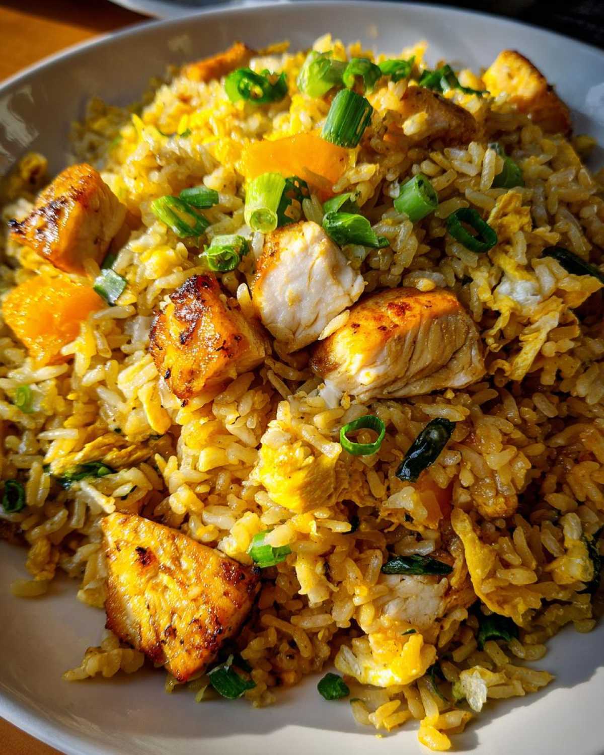 A close-up, brightly lit bowl of Gluten-Free Lemon Pepper Fried Rice featuring golden rice, seared chicken chunks, and green onions.