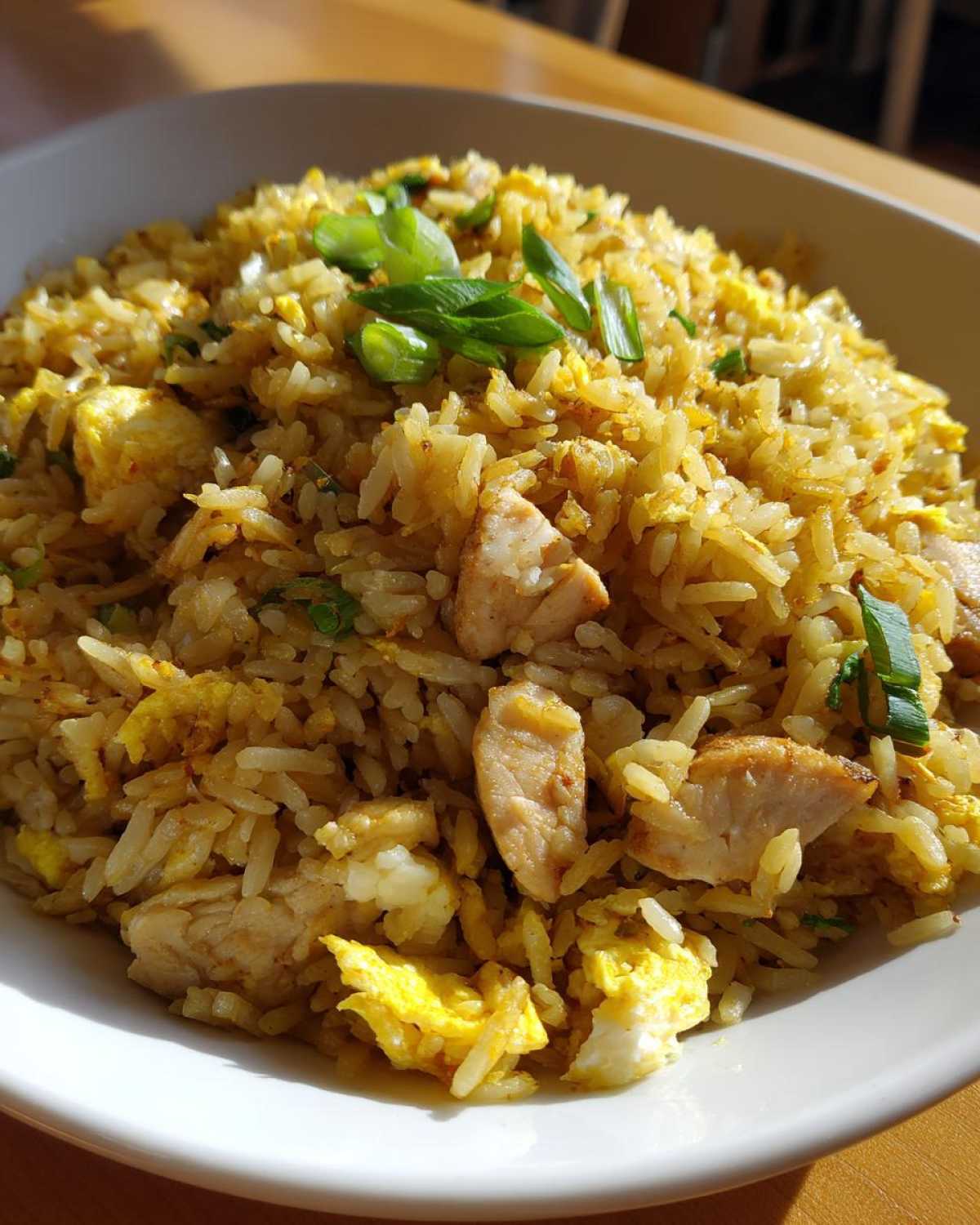 Close-up of a white bowl filled with Gluten-Free Lemon Pepper Fried Rice mixed with chunks of chicken and scrambled egg, topped with green onions.