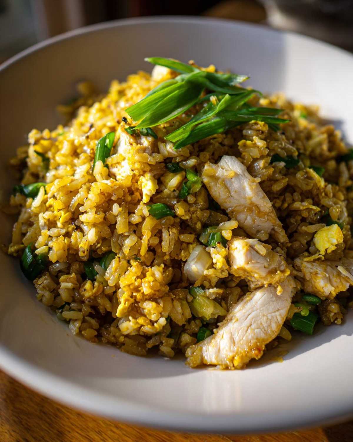 Close-up of a bowl filled with golden Gluten-Free Lemon Pepper Fried Rice mixed with scrambled egg and topped with sliced chicken breast and green onions.