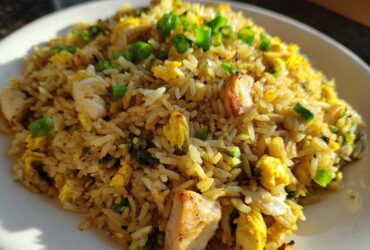 A close-up of a plate piled high with Gluten-Free Lemon Pepper Fried Rice featuring chunks of chicken and scrambled egg, topped with green onions.