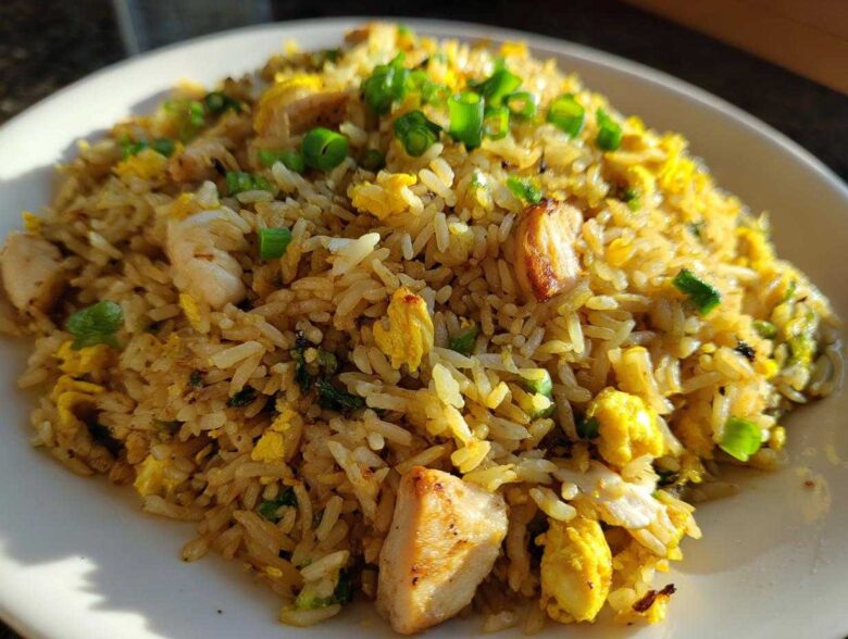 A close-up of a plate piled high with Gluten-Free Lemon Pepper Fried Rice featuring chunks of chicken and scrambled egg, topped with green onions.
