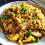 Close-up of a bowl of savory Gluten-Free Lemon Pepper Fried Rice with visible pieces of chicken and scrambled egg, topped with green onions.