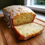 A loaf of moist Gluten-Free Lemon Zucchini Bread, partially sliced, topped with lemon glaze and zest.