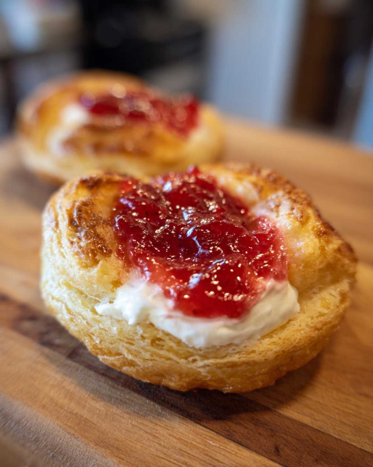 Close-up of a flaky Gluten-Free Strawberry Cream Cheese Danish topped with cream cheese and strawberry jam on a wooden board.