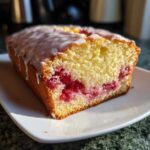 Close-up of a slice of Gluten-Free Strawberry Lemon Pound Cake showing bright red berries baked inside and topped with white glaze.