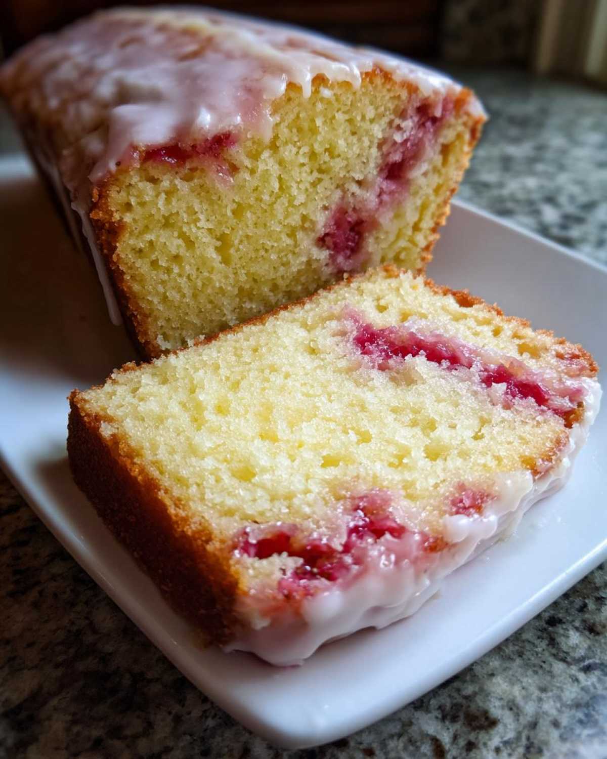 Close-up of a slice of Gluten-Free Strawberry Lemon Pound Cake showing moist crumb and pink strawberry pieces, topped with white glaze.