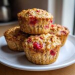 A stack of four golden-brown Gluten-Free Strawberry Oat Muffins studded with bright red strawberries on a white plate.