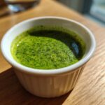Close-up of vibrant Green Goddess Salad Dressing, freshly blended, served in a small white ramekin on a wooden table.