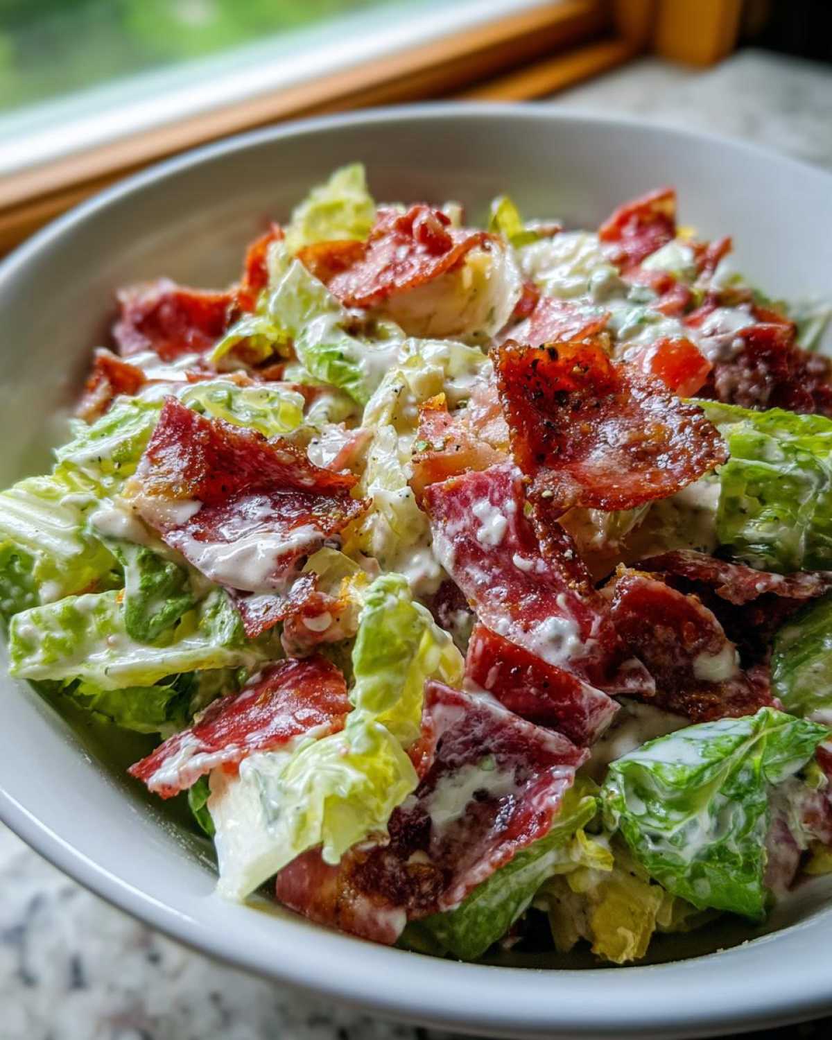 A close-up of a bowl filled with a creamy grinder salad featuring crisp lettuce, chunks of meat, and creamy dressing.