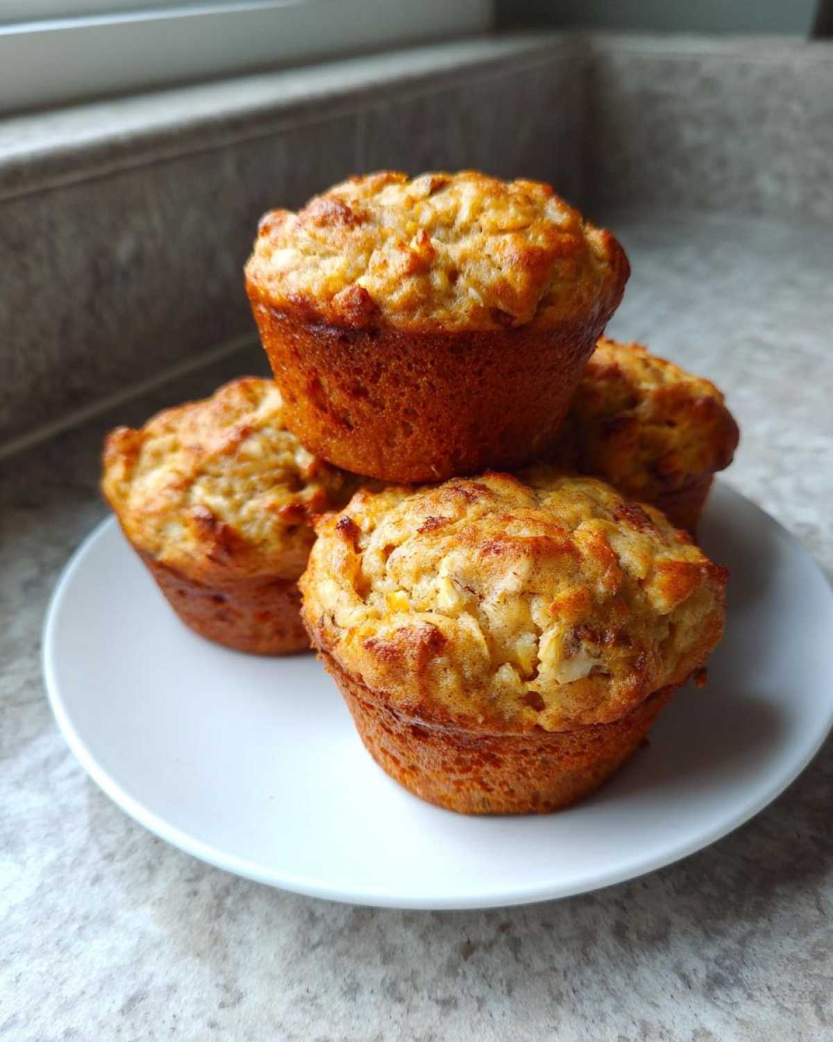 Four golden-brown High Protein Banana Muffins stacked on a white plate, perfect for breakfast.