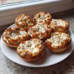 Seven baked High-Protein Cottage Cheese Bagel Bites topped with everything bagel seasoning on a white plate.
