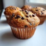 A close-up, appetizing photo of a freshly baked Homemade Chocolate Chip Muffins with a golden top studded with chocolate chips.