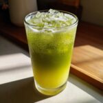 A tall glass filled with a vibrant, layered Iced Matcha Pineapple Refresher, topped with ice cubes.