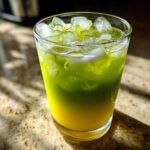 A tall glass filled with a layered Iced Matcha Pineapple Refresher, showing bright yellow pineapple juice below vibrant green matcha, topped with ice.
