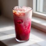 A tall glass filled with a layered Iced Raspberry Vanilla Chai, showing bright red raspberry syrup mixing with creamy white chai.