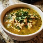 A close-up of a white bowl filled with vibrant Instant Pot Chicken Pozole Verde, topped with shredded chicken and fresh cilantro.