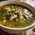 Close-up of a white bowl filled with rich, green broth, shredded chicken, and fresh cilantro for Instant Pot Chicken Pozole Verde.