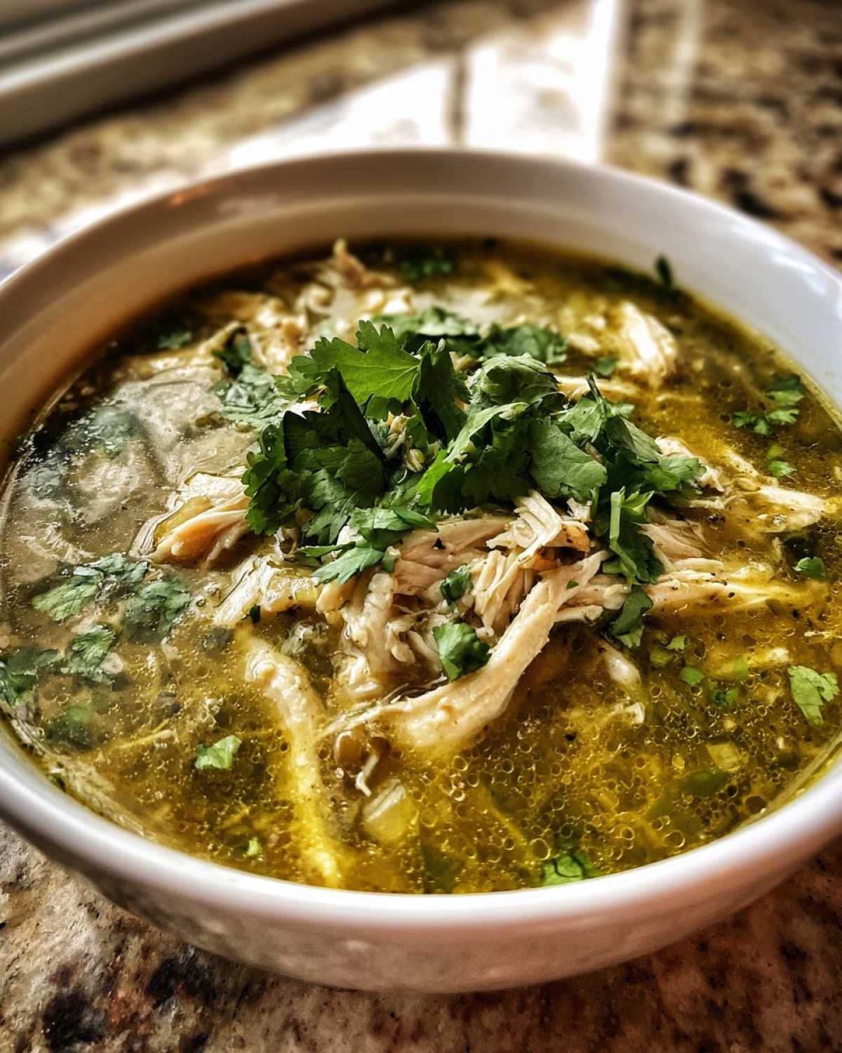 Close-up of a white bowl filled with vibrant green broth, shredded chicken, and topped generously with fresh cilantro for Instant Pot Chicken Pozole Verde.