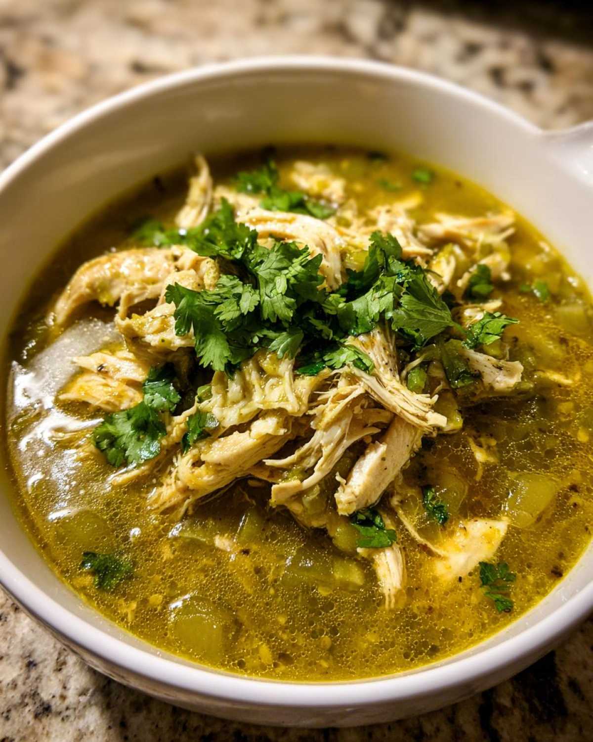 A close-up of a white bowl filled with rich, green Instant Pot Chicken Pozole Verde, topped with shredded chicken and fresh cilantro.