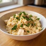 A white bowl filled with Instant Pot Creamy Chicken and Orzo, topped with fresh chopped parsley.