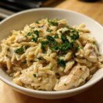 A close-up of a white bowl filled with Instant Pot Creamy Chicken and Orzo, topped with fresh parsley.