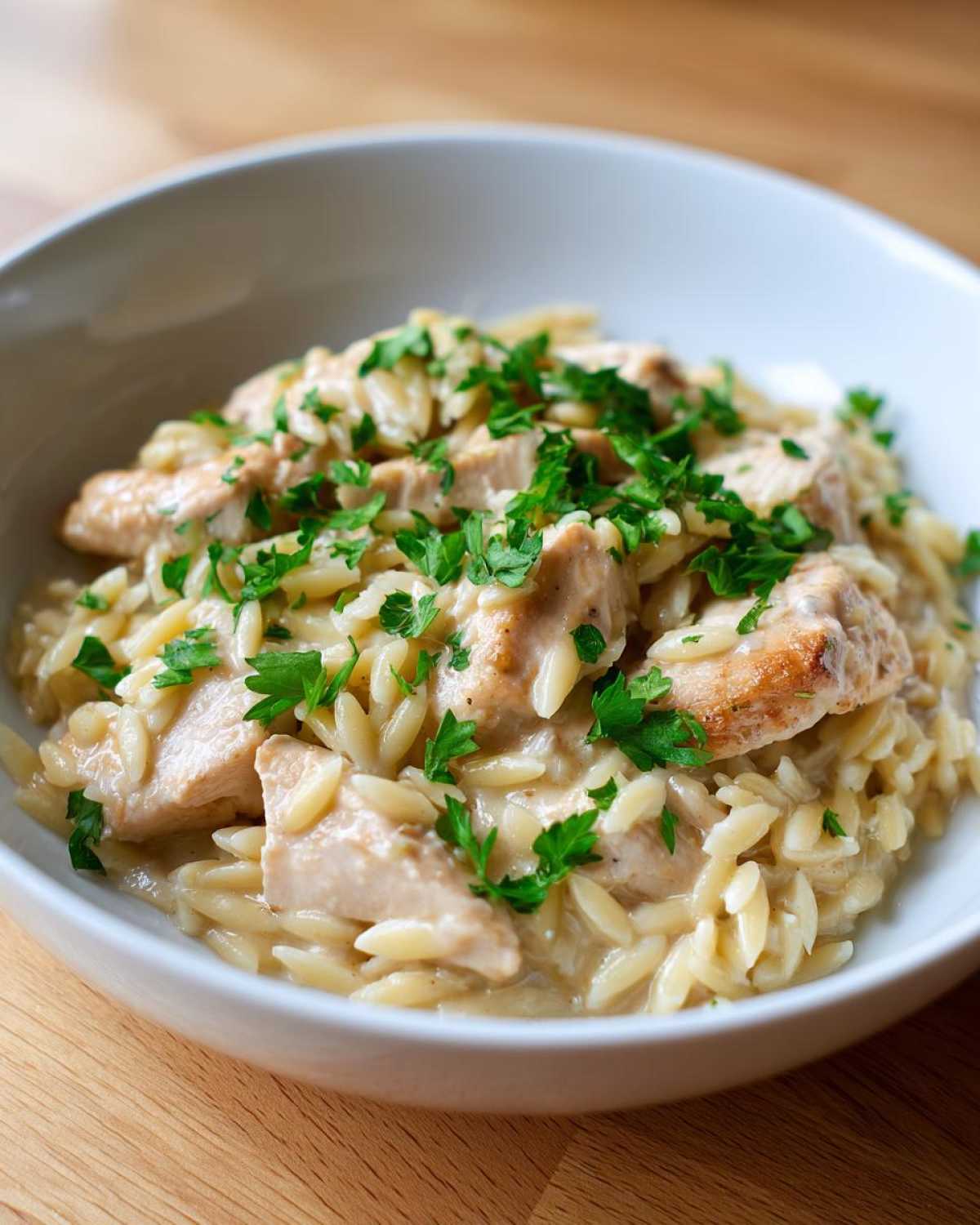 A close-up of Instant Pot Creamy Chicken and Orzo served in a white bowl, topped with fresh parsley.