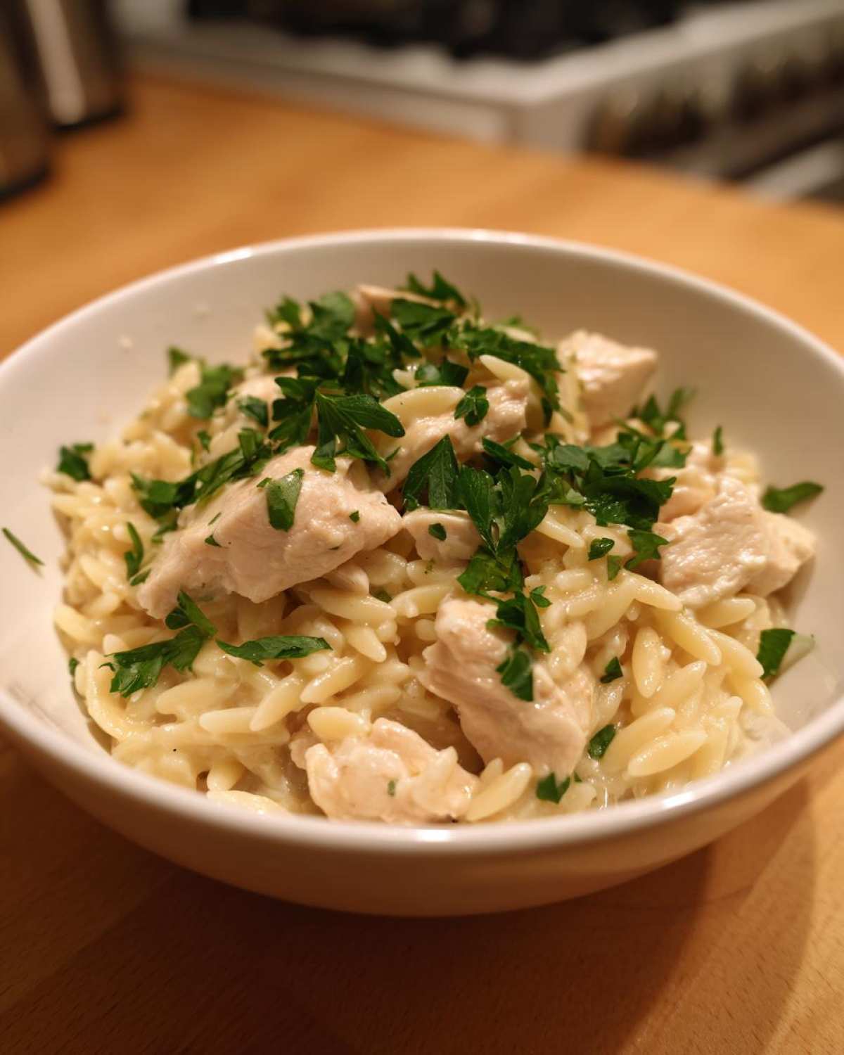 A close-up of a white bowl filled with Instant Pot Creamy Chicken and Orzo, topped with fresh parsley.