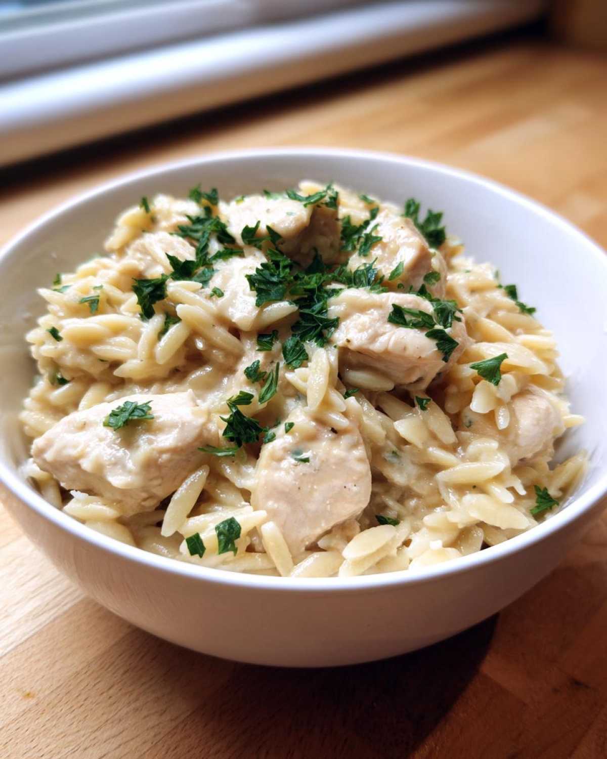 Close-up of a white bowl filled with Instant Pot Creamy Chicken and Orzo, garnished with fresh parsley.